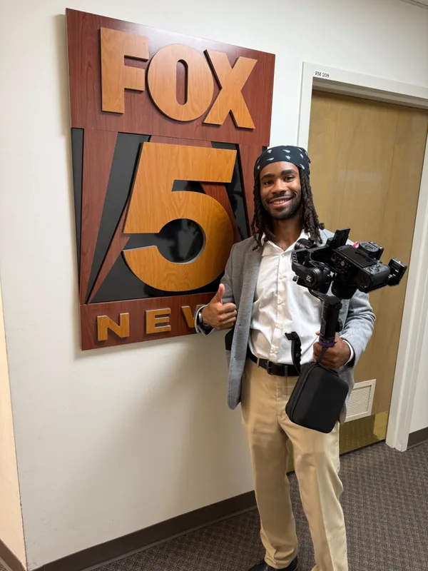 Julian Bass holding a camera rig beside a FOX 5 sign.
